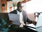 man looks at document in front of laptop