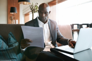 man looks at document in front of laptop